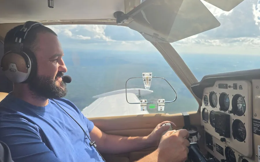 Justin, a veteran, at the controls in the left seat of a single-engine airplane during a VA Ready sponsored discovery flight, headset on and hands on the yoke, with the Georgia landscape below